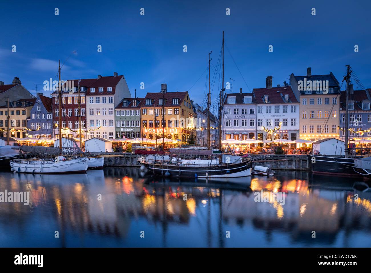 Edifici colorati e barche alte con alberi sul lungomare di Nyhavn al tramonto, canale Nyhavn, Nyhavn, Copenaghen, Danimarca, Europa Foto Stock