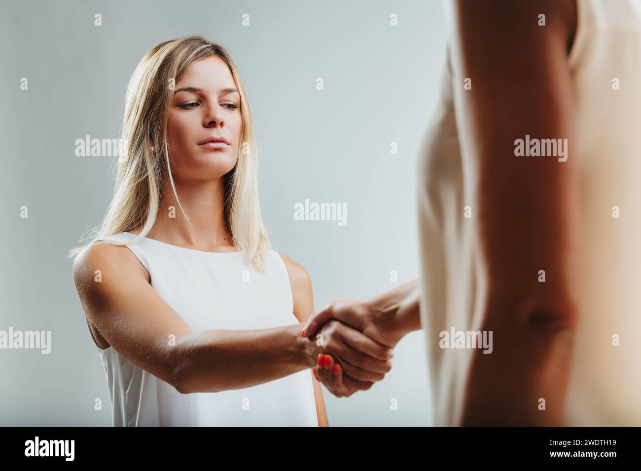 Stretta di mano con esitazione, l'espressione di una donna rivela incertezza, forse nascondendo pensieri preoccupanti Foto Stock