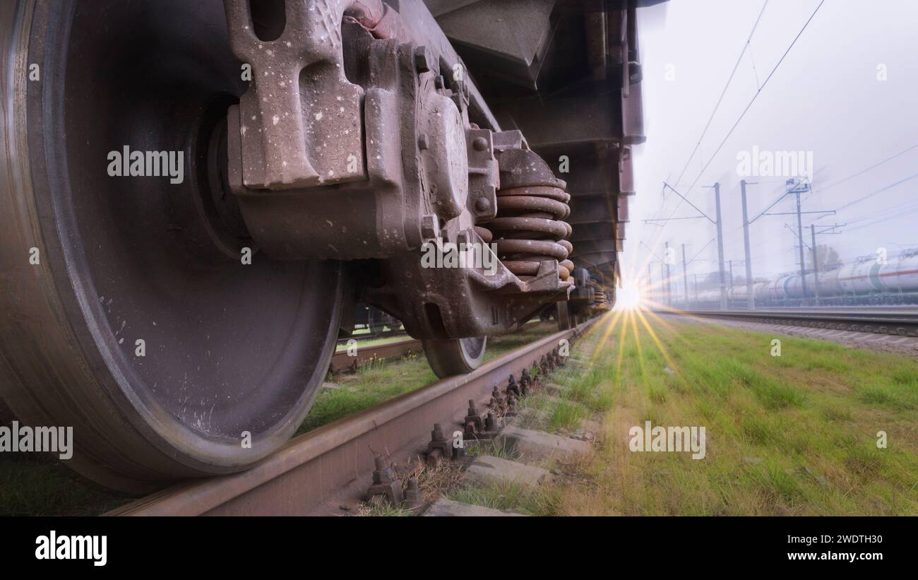 Vista dal basso delle ruote di un treno che si muove velocemente su una ferrovia. Consegna rapida delle merci per ferrovia. Lo sfondo sfocato crea l'effetto del movimento. Foto Stock
