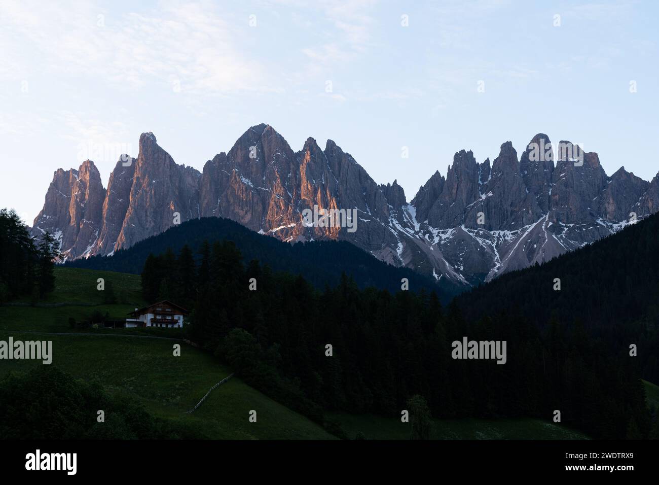 Serenità alpina: Prima luce sulle cime robuste della Val di Funes, Italia, con un Mountain Chalet solitario Foto Stock