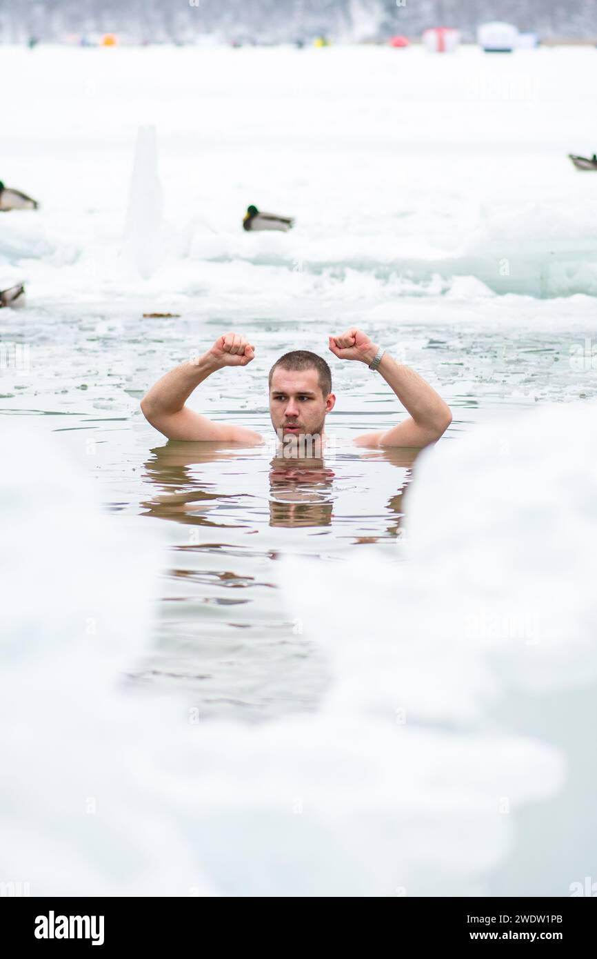 Bel ragazzo o uomo che fa il bagno di ghiaccio nell'acqua gelida di un lago ghiacciato tra le anatre. Metodo Wim Hof, terapia a freddo, tecniche respiratorie, verticale Foto Stock