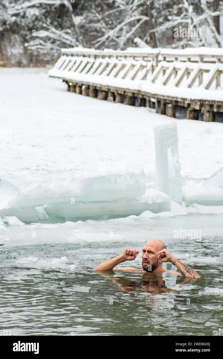 Bel ragazzo o uomo che fa il bagno di ghiaccio nell'acqua gelida di un lago ghiacciato tra le anatre. Metodo Wim Hof, terapia a freddo, tecniche respiratorie, verticale Foto Stock