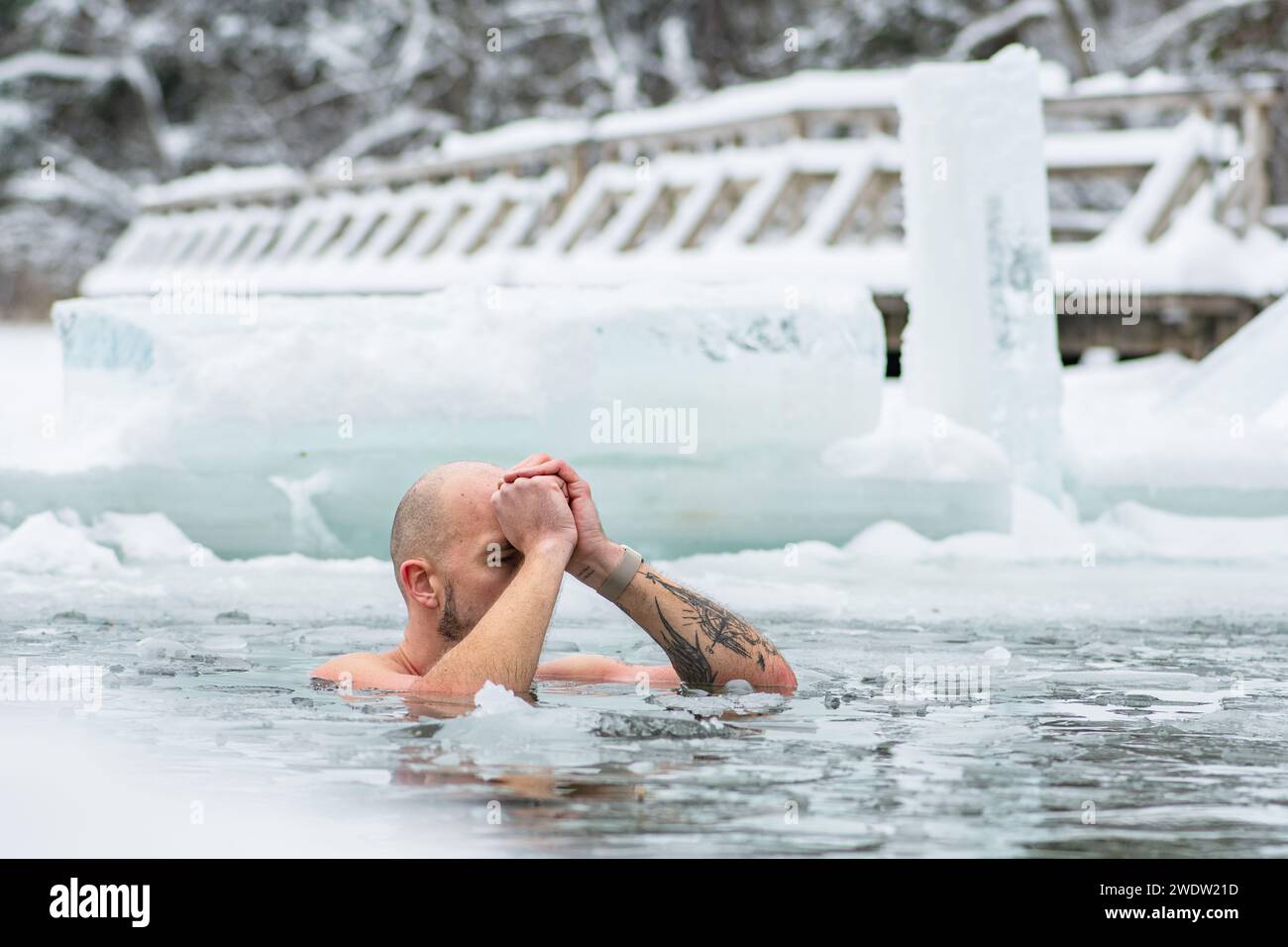 Bel ragazzo o uomo che fa il bagno di ghiaccio nell'acqua gelida di un lago ghiacciato tra le anatre. Metodo Wim Hof, terapia fredda, tecniche di respirazione Foto Stock