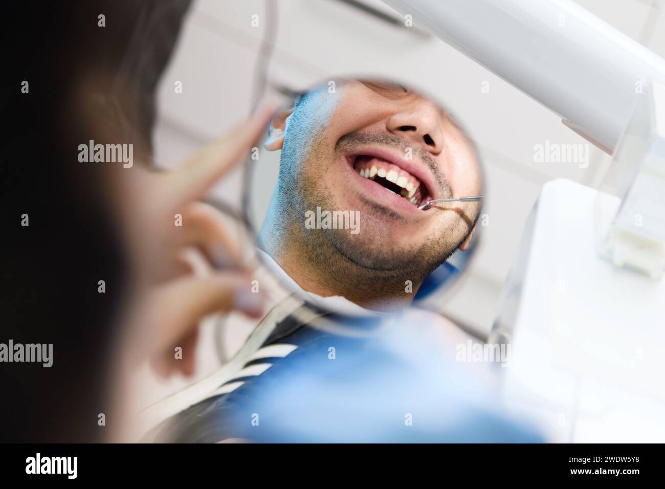 Un paziente esamina il suo sorriso in uno specchio durante un controllo dentale, mostrando una visione ravvicinata e personale delle cure odontoiatriche moderne Foto Stock