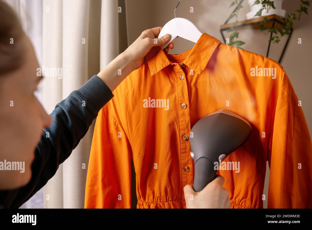 donna che stira un vestito con un sistema di stiratura a vapore a casa Foto Stock