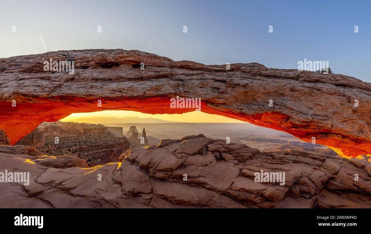 Il Mesa Arch nel Parco Nazionale delle Canyonlands è illuminato in arancione dal sole dal basso durante l'alba. Foto Stock