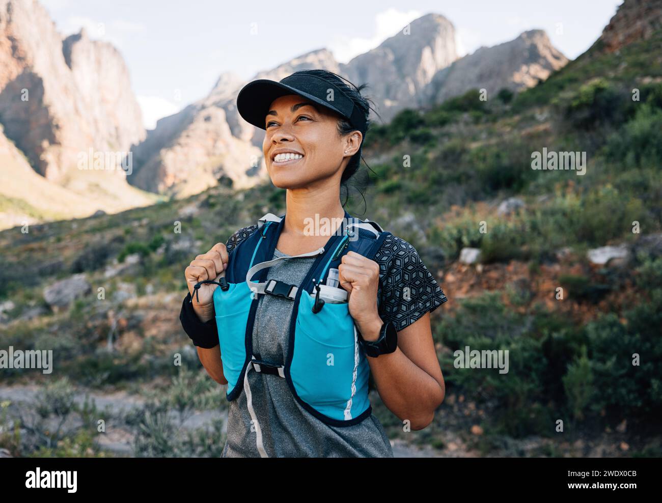 Sorridente donna di mezza età che si rilassa durante un'escursione, godendosi la vista. Donna che indossa abbigliamento sportivo da trekking che guarda sulle montagne. Foto Stock