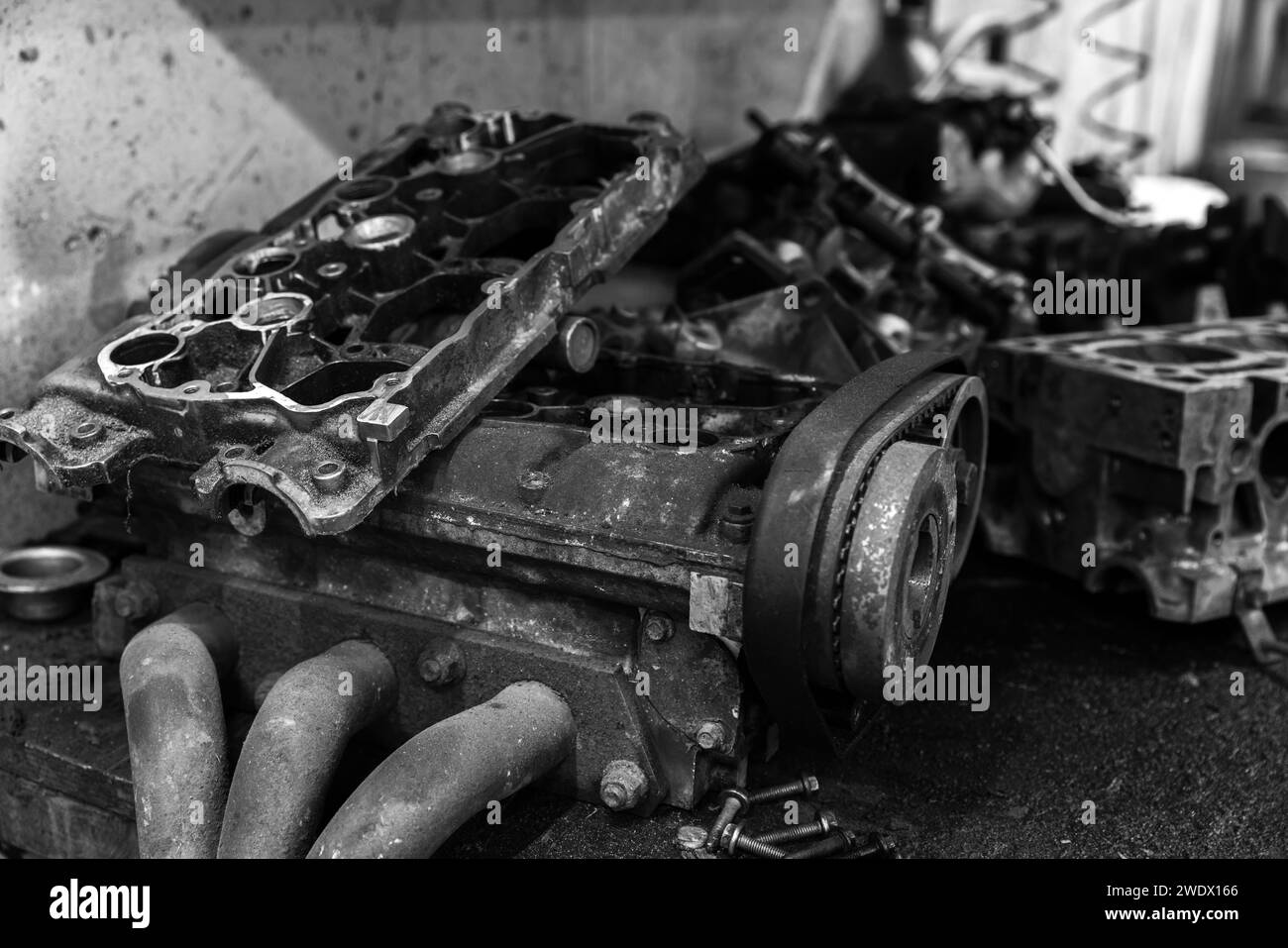 Le parti del motore dell'auto rotte si trovano su un tavolo sporco in un'officina di riparazione auto, foto in bianco e nero Foto Stock
