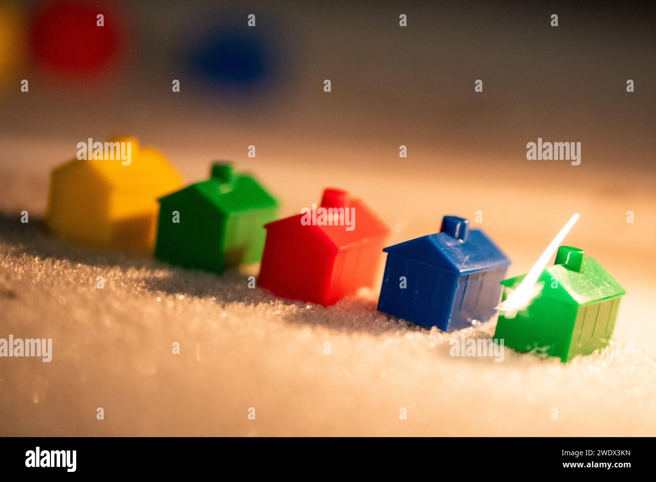 Una fila di case in miniatura su una superficie ricoperta di gelo con scintille di luce che infiammano la casa verde Foto Stock