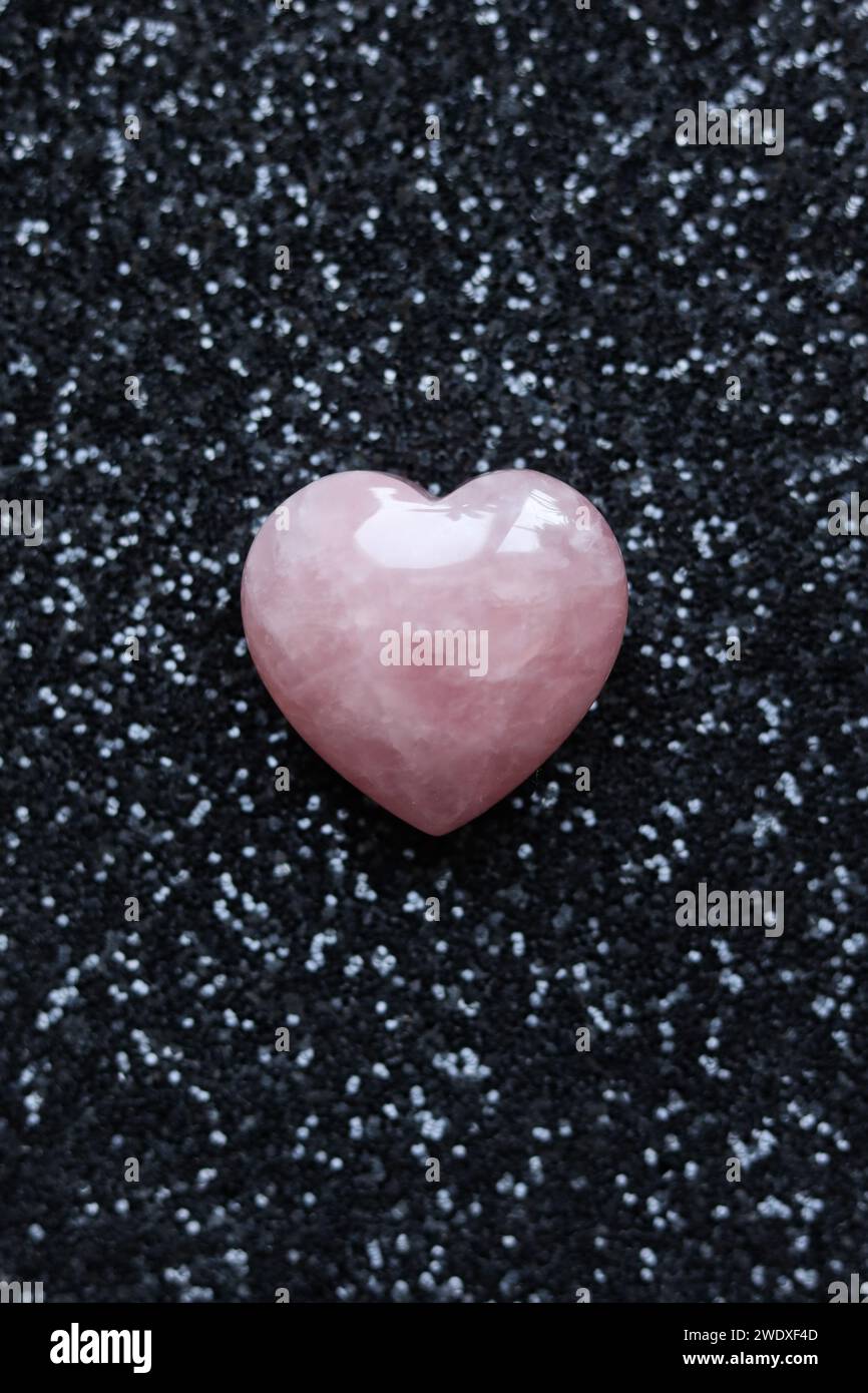 cuore di quarzo rosa su sfondo nero glitter, concetto di san valentino. Foto Stock