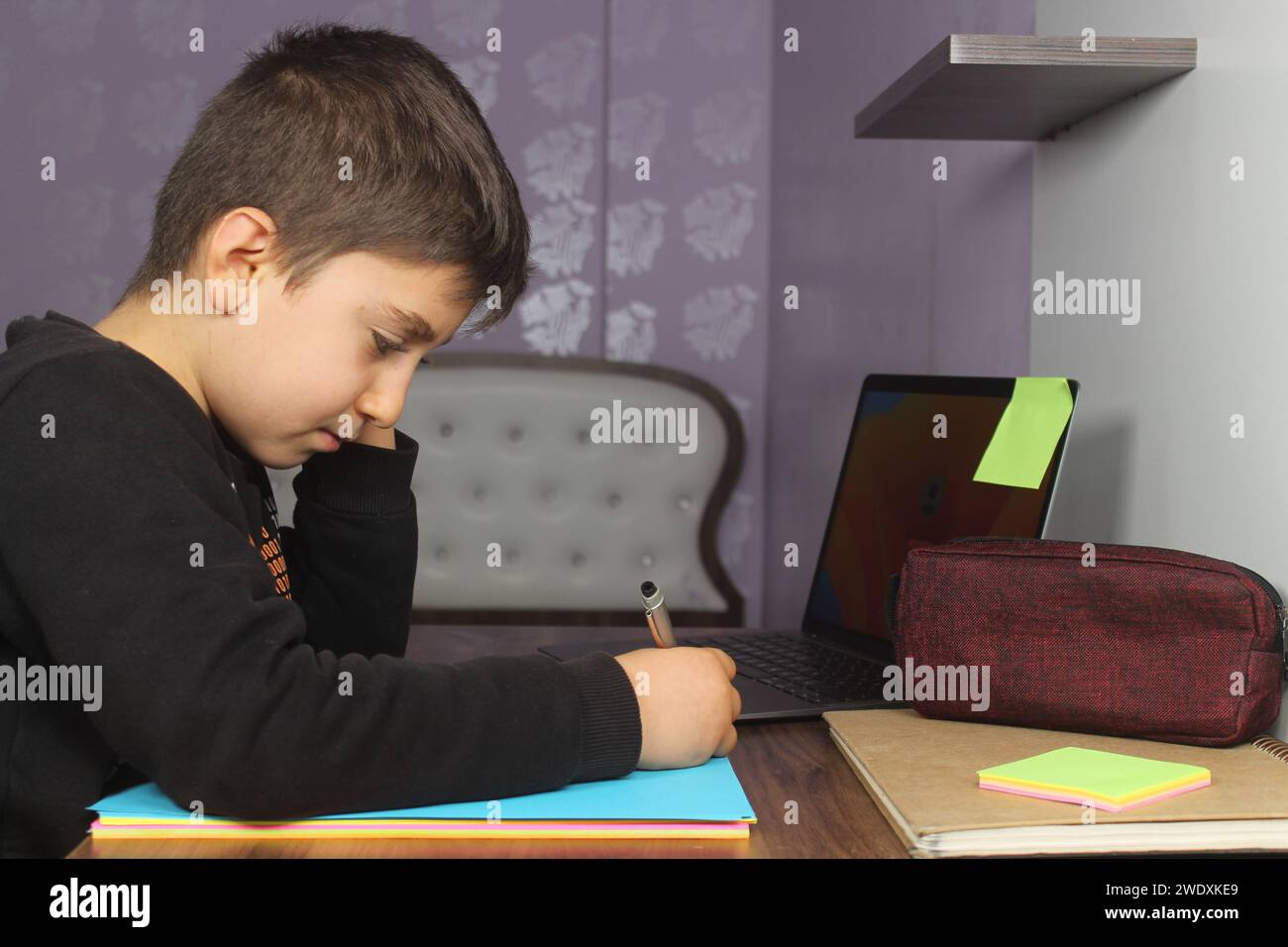 Formazione a distanza online. Scolaro studia a casa e fa i compiti a scuola. Studente annoiato che cerca di scrivere composizione. Resta a casa. Foto Stock