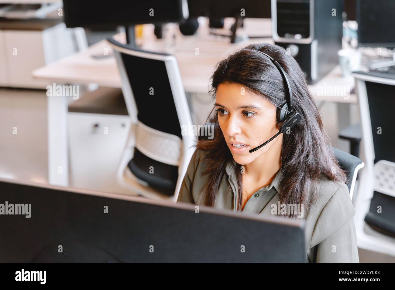 Rappresentante dell'assistenza clienti femminile dedicata con cuffie presso una postazione di lavoro. Foto Stock