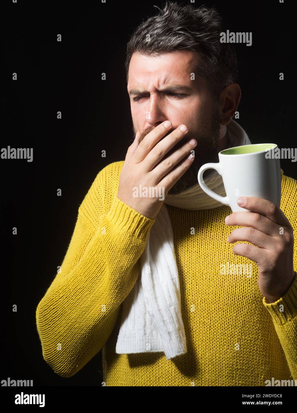 Uomo malato in maglione avvolto in sciarpa con una tazza di tè medicinale. Bel ragazzo che ha mal di gola. Uomo malbarbato con influenza e febbre che beve guarigione Foto Stock