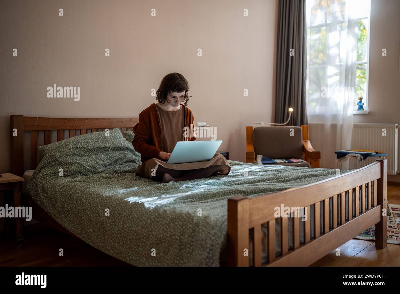 Giovane freelance che lavora su un computer portatile seduto a letto a casa. Foto Stock