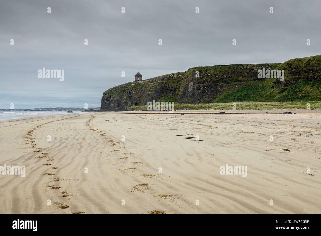 Paesaggio di spiaggia con impronte verso una torre medievale sopra la scogliera sulla costa nord nella contea di Antrim, Irlanda del Nord, Regno Unito Foto Stock