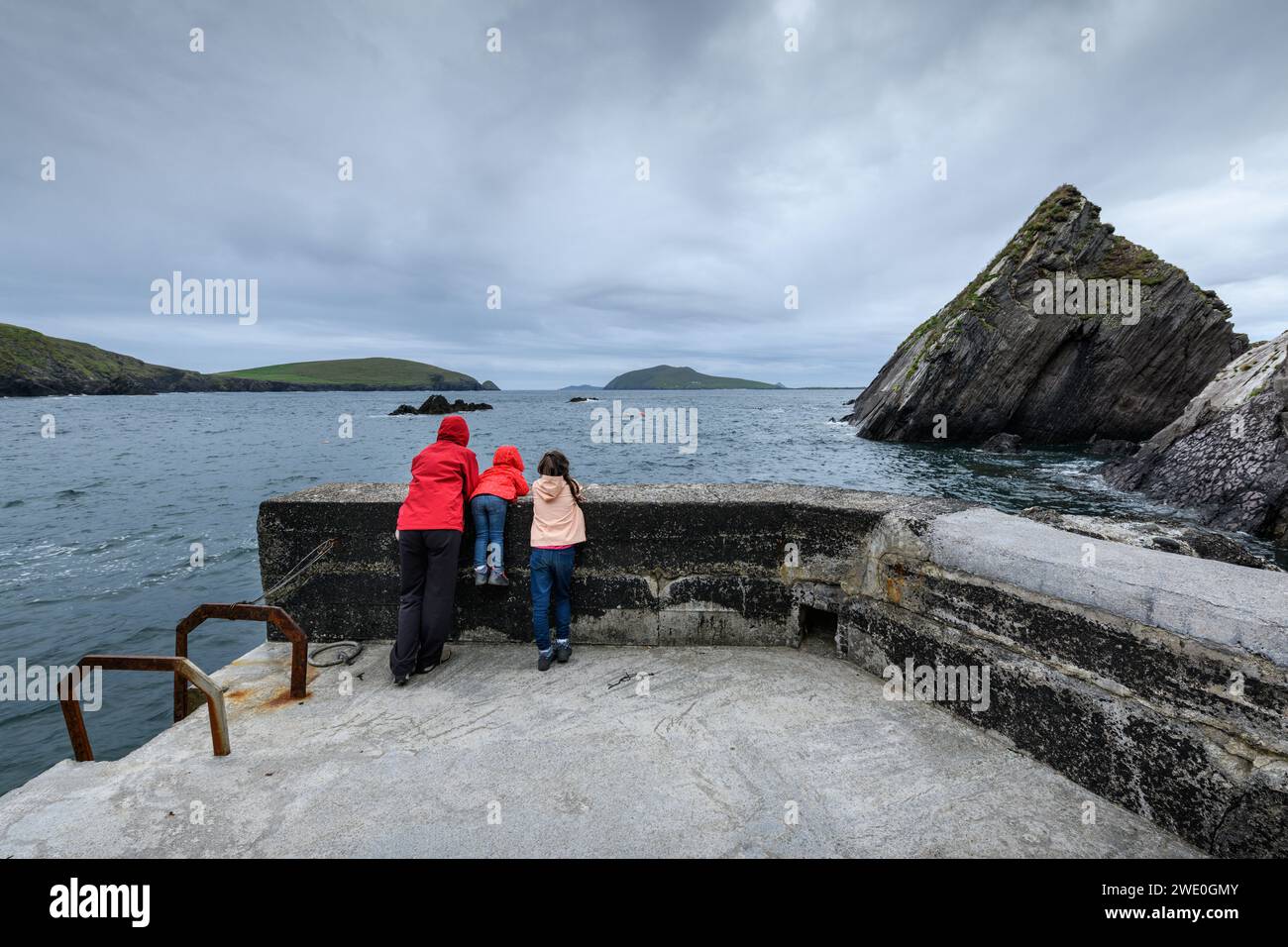 Due ragazze e un bambino che guardano fuori da un punto di osservazione sulla riva del Dingle Ring con uno spettacolare paesaggio marino in una giornata di pioggia, Kerry, Irlanda Foto Stock