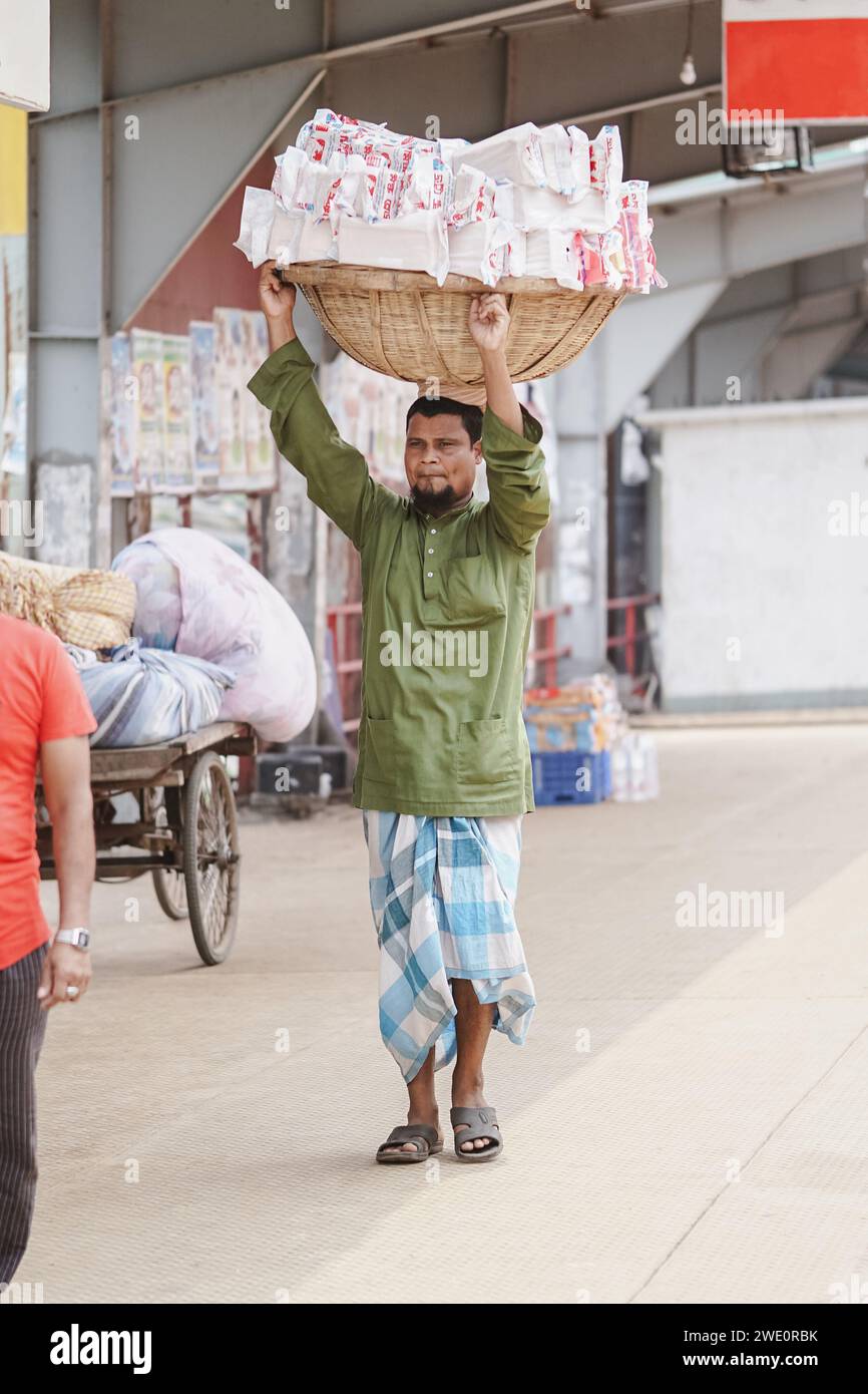 Uomo del Bangladesh che porta un cesto di pane sulla testa nel terminale di lancio di Sadarghat (Sadarghat, Dacca, Bangladesh 09-05-2023) Foto Stock