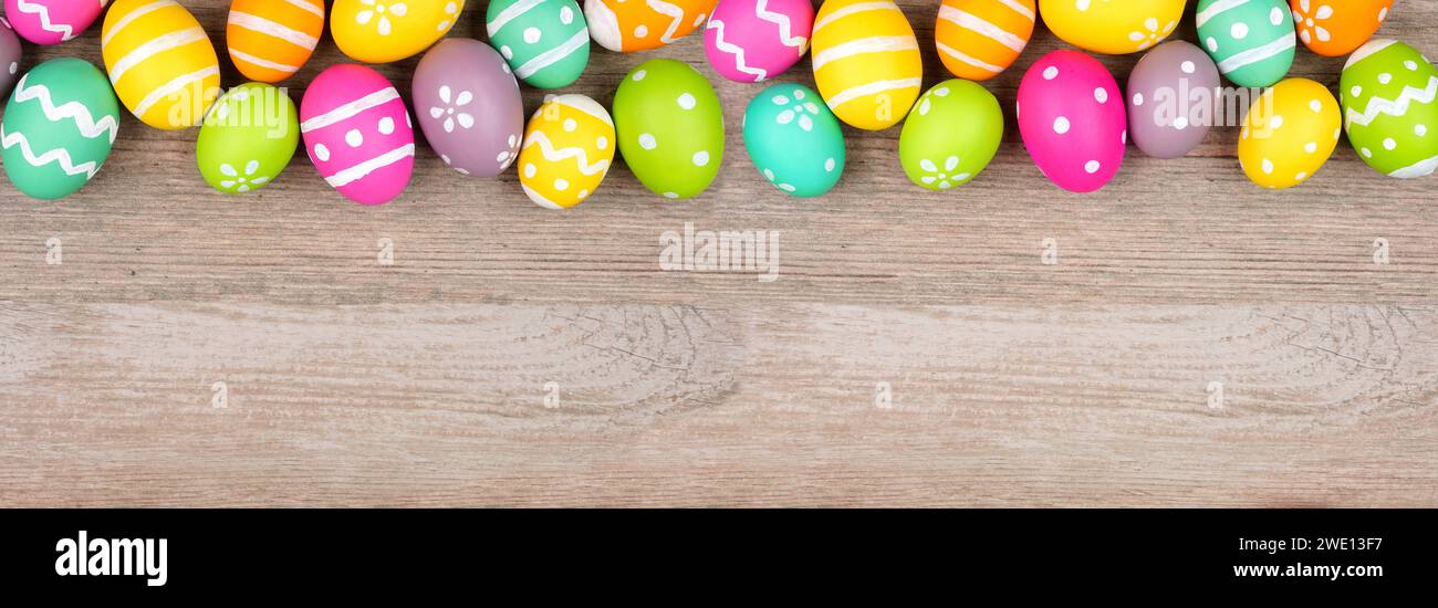 Colorato bordo superiore dell'uovo di Pasqua. Vista dall'alto su uno sfondo banner di legno chiaro. Copia spazio. Foto Stock