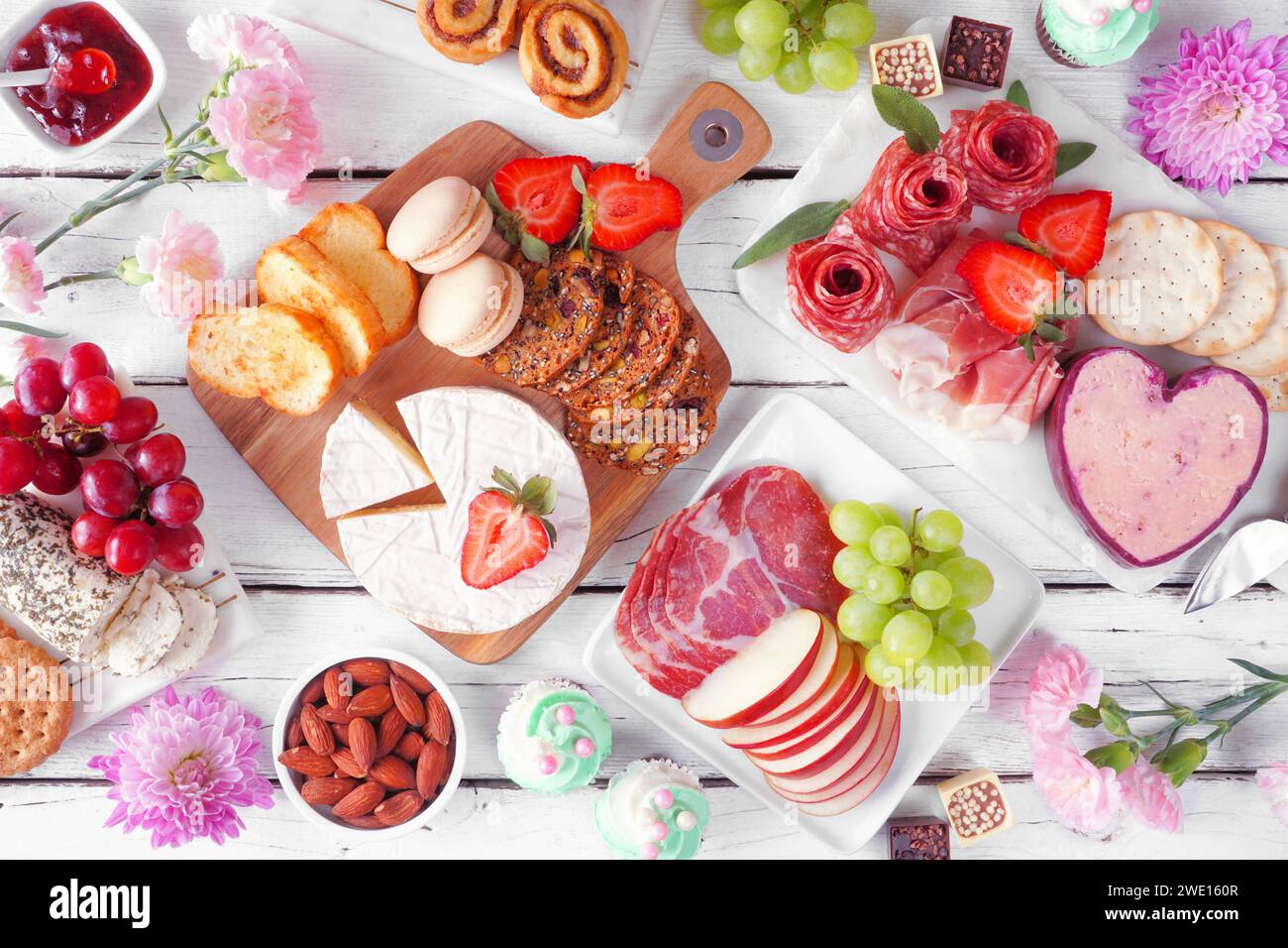 Scena da tavolo a tema Festa della mamma su uno sfondo di legno bianco. Varietà di formaggi, salumi, frutta e dolci. Vista dall'alto. Foto Stock