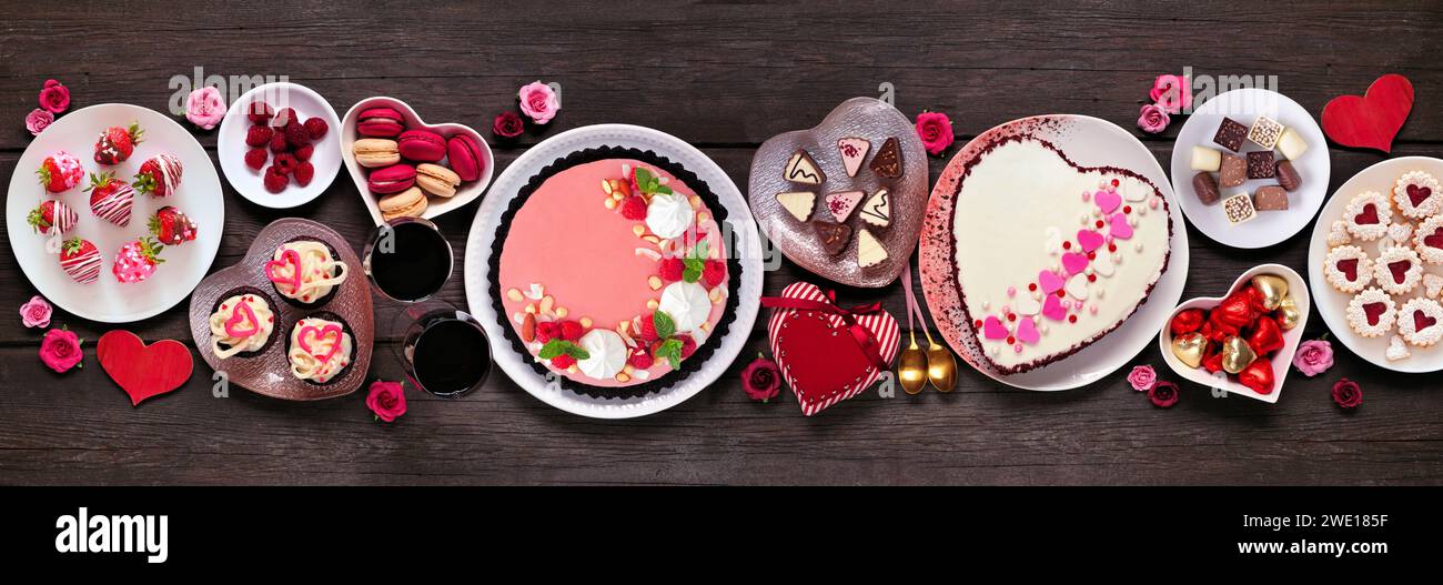 Cena di San Valentino con dessert e dolci assortiti. Vista dall'alto su uno sfondo banner di legno scuro. Tema dell'amore e del cuore. Foto Stock