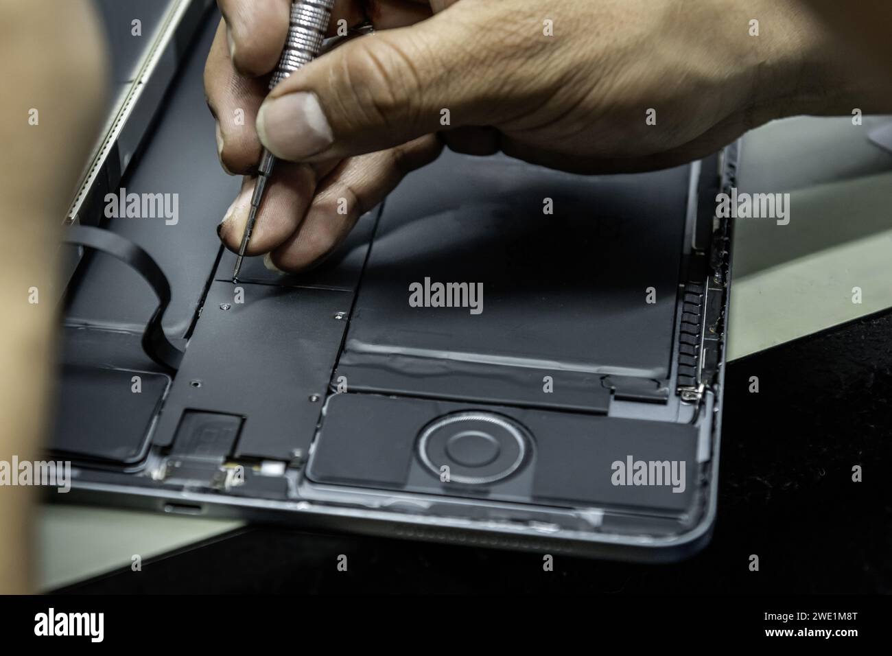 Un tecnico di un'officina di riparazione elettronica che avvita le parti in una riparazione di tablet con le sue piccole viti Foto Stock