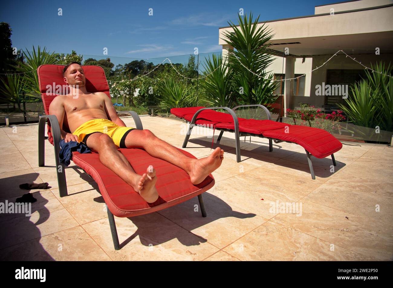 Uomo maturo sdraiato sulla chaise longue vicino alla piscina Foto Stock