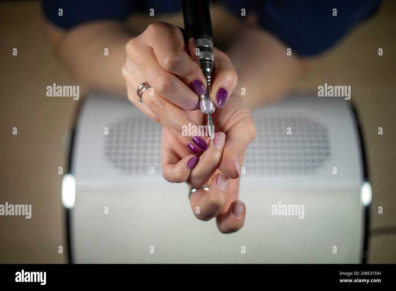 Primo piano dettagliato di una donna irriconoscibile che rimuove il suo smalto per unghie con lima elettrica su un collettore di polveri, primo piano della manicure fai da te Foto Stock