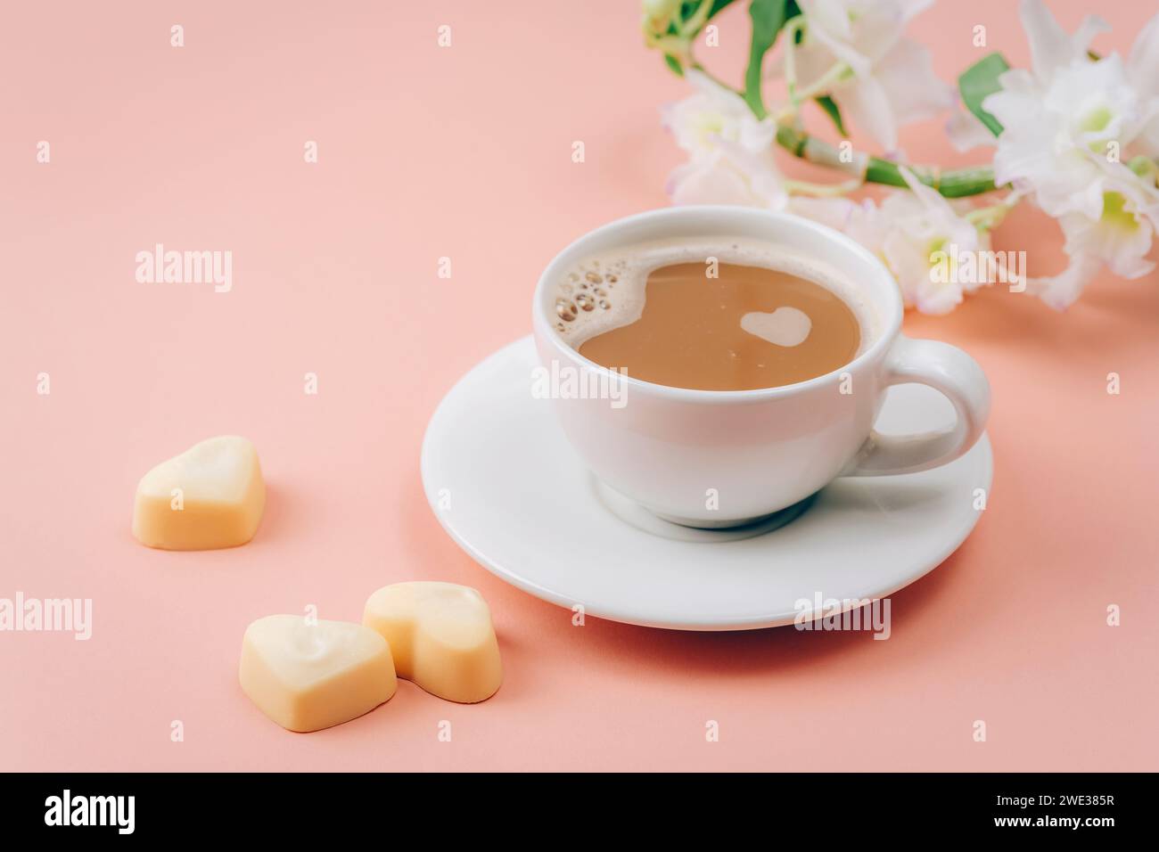 Tazza di caffè, caramelle a forma di cuore e fiori bianchi su sfondo rosa. Concetto di San Valentino. Primo piano. Foto Stock
