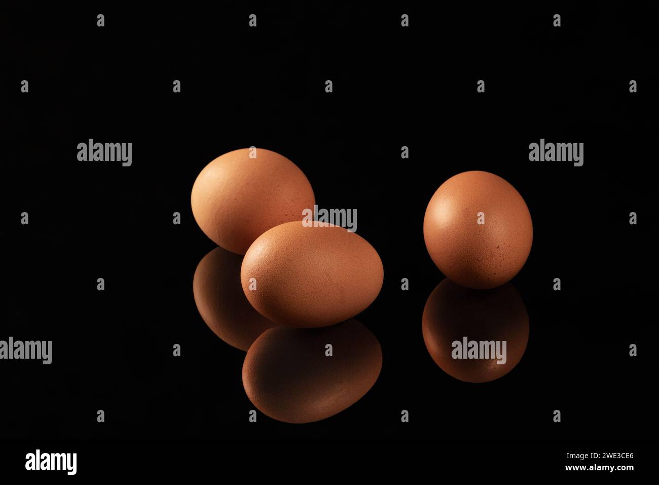 Un'immagine visivamente sorprendente che cattura il riflesso delle uova di gallina marroni su una superficie lucida e nera a specchio, creando una c Foto Stock