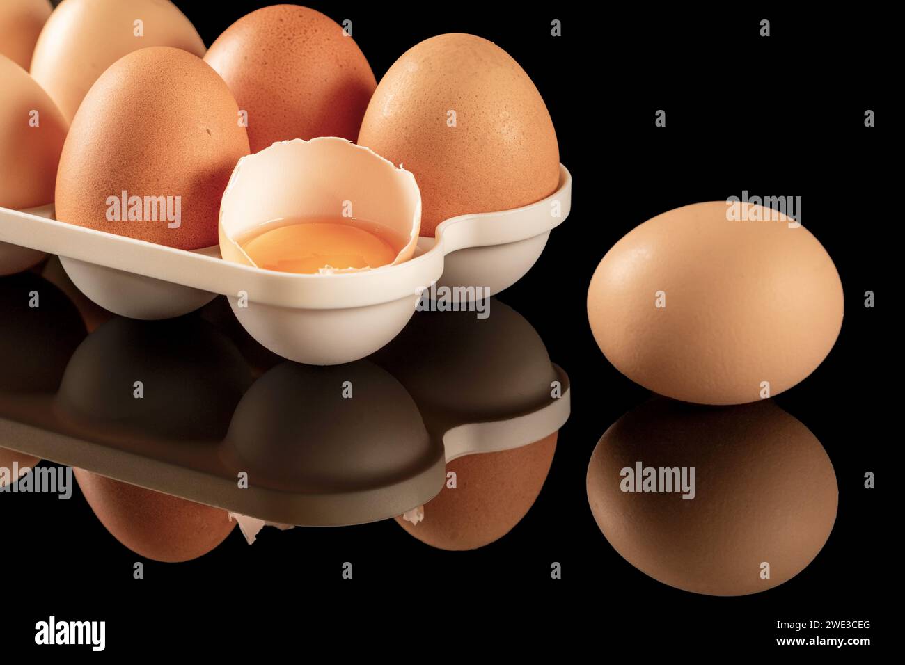 Un'immagine ravvicinata delle uova di gallina marroni esposte su una superficie nera a specchio. Le uova si riflettono sullo sfondo lucido e riflettente, creando un Foto Stock