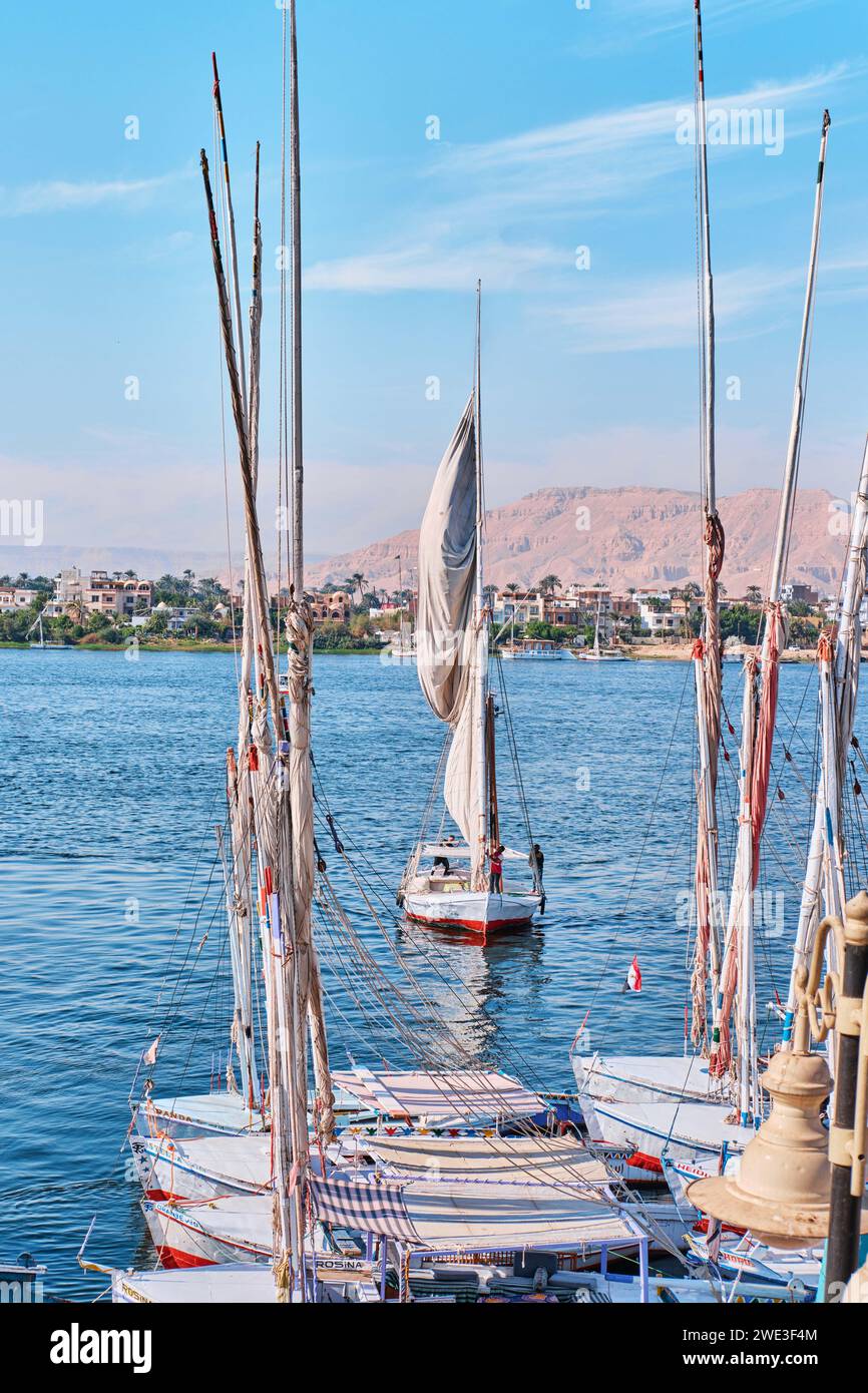 Luxor, Egitto - dicembre 26 2023: Tradizionali traghetti a motore e barche a vela in feluca ormeggiate lungo il Nilo Foto Stock