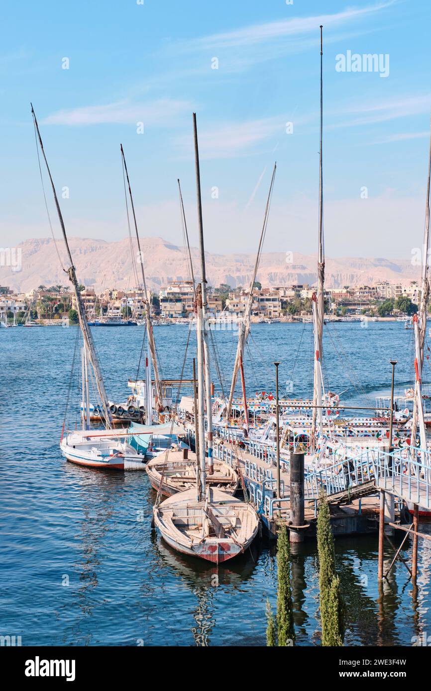 Luxor, Egitto - dicembre 26 2023: Tradizionali traghetti a motore e barche a vela in feluca ormeggiate lungo il Nilo Foto Stock