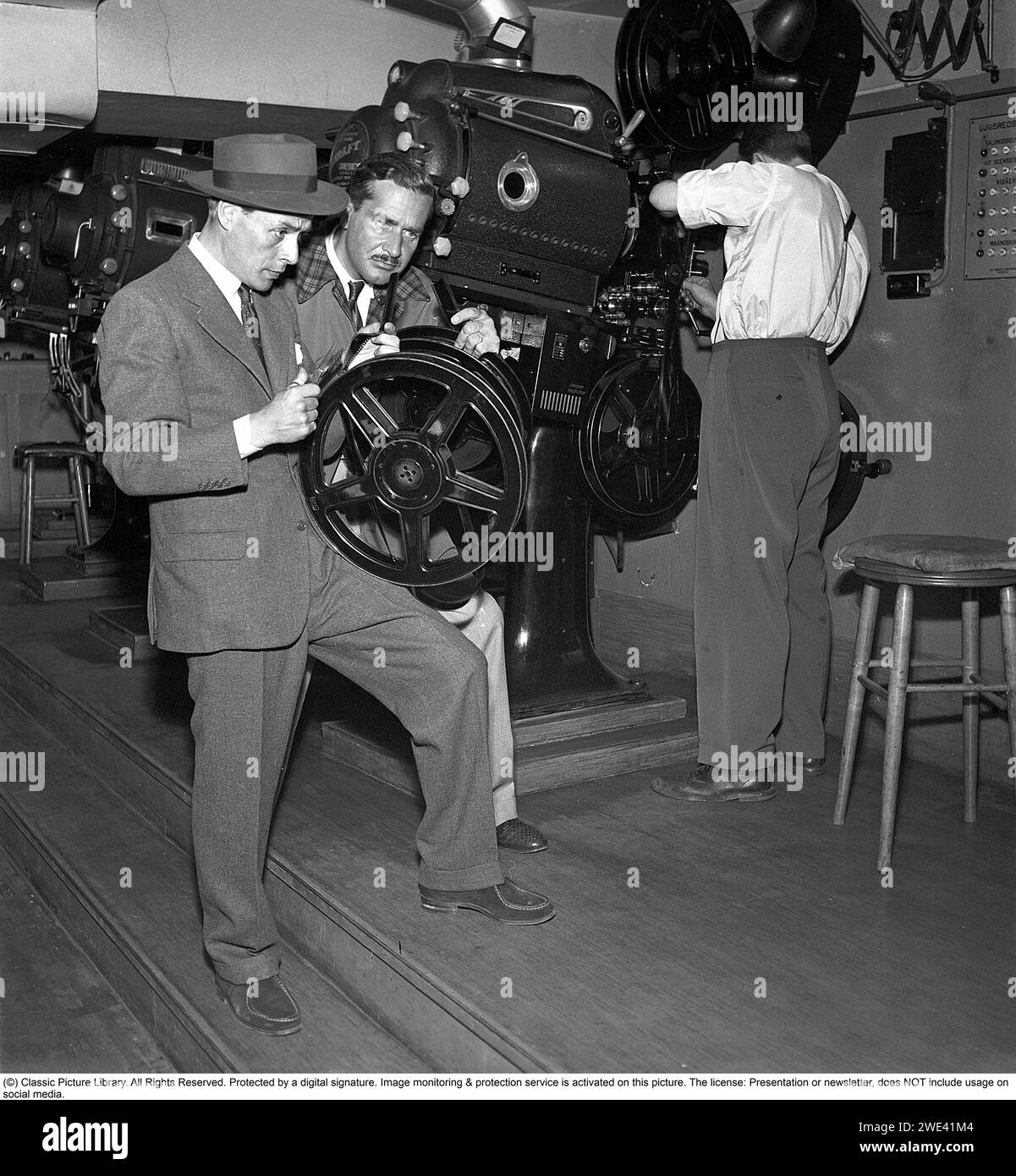 Hasse Ekman. 1915-2004. Attore e regista svedese. Qui con il produttore Lorens Marmstedt. 1908-1966 in una sala di proiezione cinematografica. Si trovano nella sala proiettore di un cinema e guardano da vicino la striscia di un filmato da mostrare nel proiettore. 1952. Kristoffersson rif. BG91-5 Foto Stock