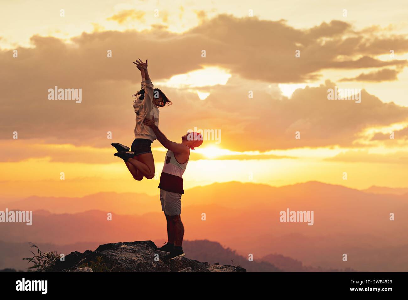 Le giovani coppie si divertono in cima alla montagna all'ora del tramonto. L'uomo sta lanciando una donna felice contro il cielo del tramonto Foto Stock