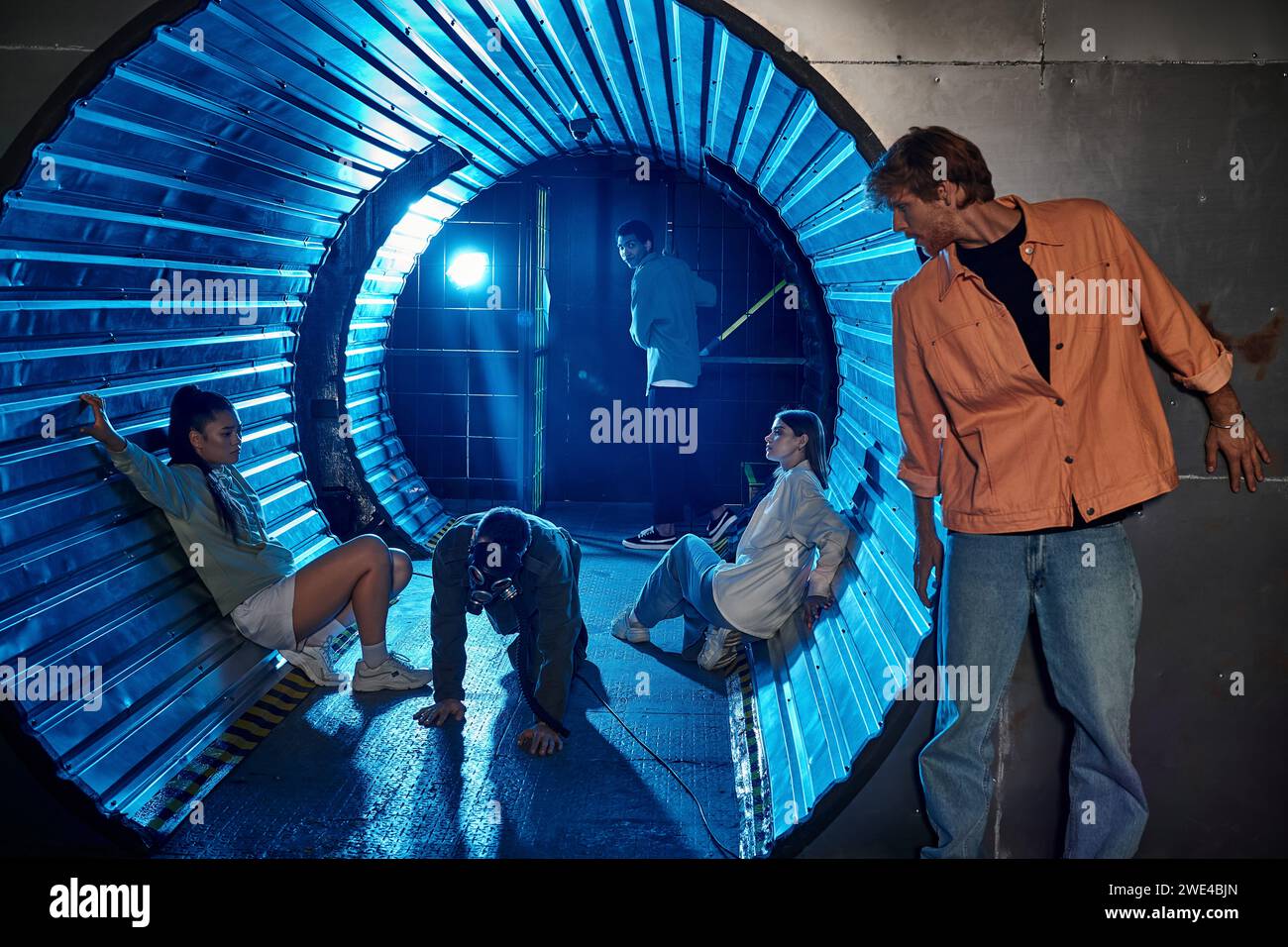 gruppo eterogeneo di amici che partecipano a un'emozionante avventura in camera quest in un tunnel con luce blu Foto Stock