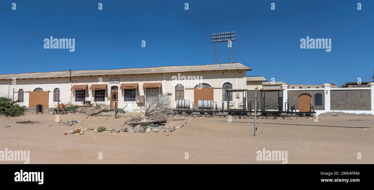 Paesaggio urbano con un trenino e edifici abbandonati nella città fantasma mineraria nel deserto, girato in tarda primavera a Kolmanskop, Namibia, Africa Foto Stock