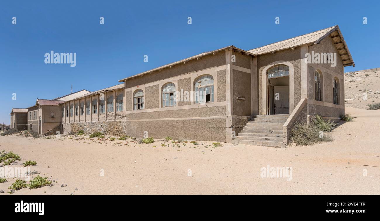 Paesaggio urbano con l'ospedale abbandonato costruito sulla sabbia nella città fantasma mineraria nel deserto, sparato con luce brillante di tarda primavera a Kolmanskop, Namibia, Africa Foto Stock