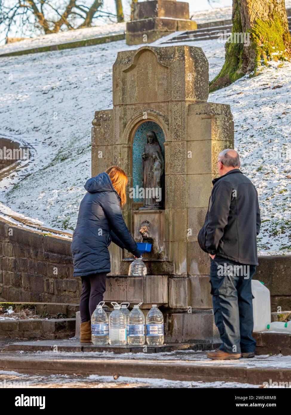 Donna che riempie bottiglie di plastica con l'acqua del pozzo di St Ann ai piedi delle piste, in inverno, nella neve. Buxton, Regno Unito Foto Stock