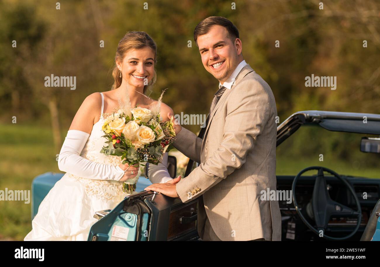 Foto divertenti, insolite, eleganti e originali con inversione di ruolo di una giovane e attraente coppia di nozze con bellissime auto veterane nella natura. Foto Stock