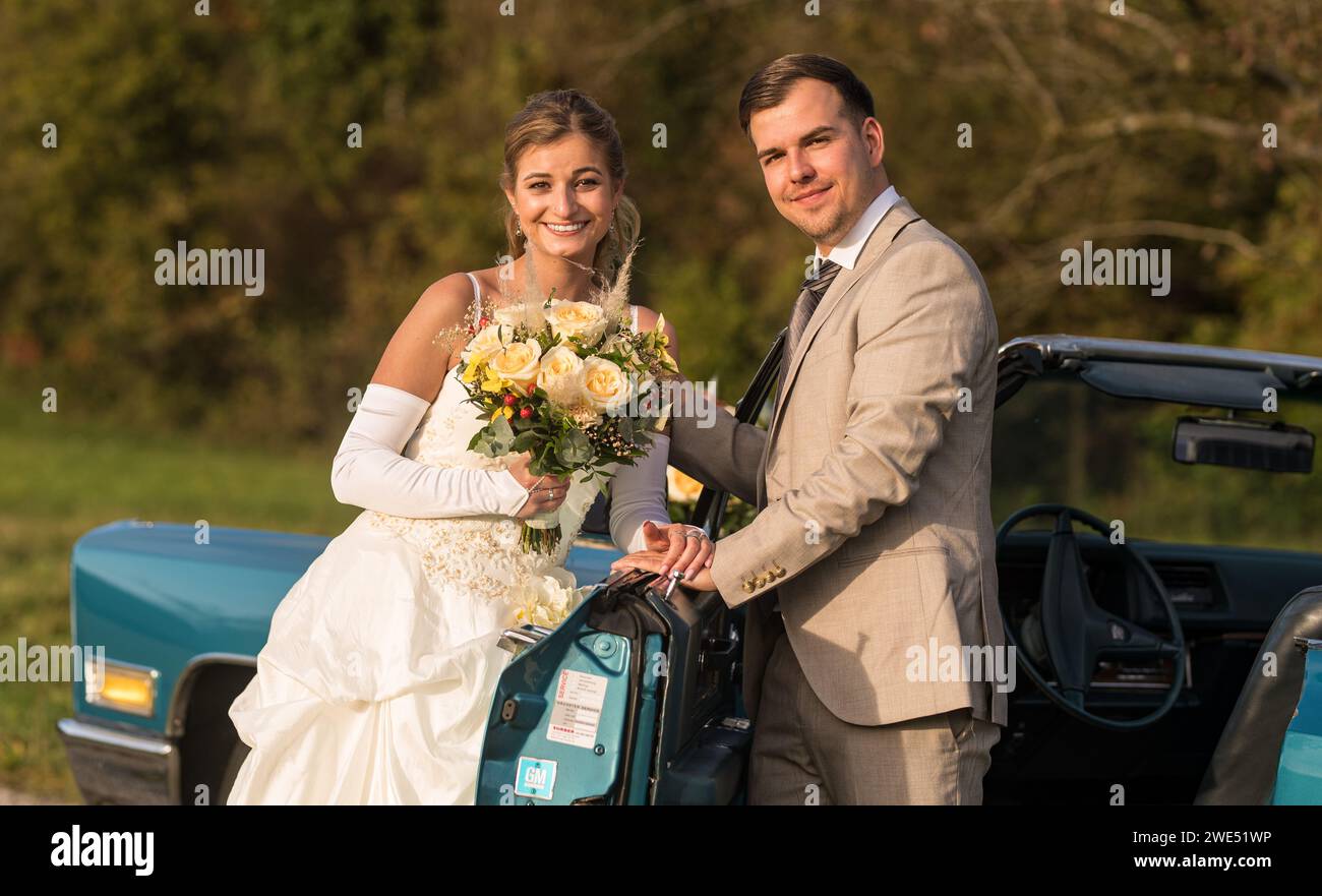Foto divertenti, insolite, eleganti e originali con inversione di ruolo di una giovane e attraente coppia di nozze con bellissime auto veterane nella natura. Foto Stock
