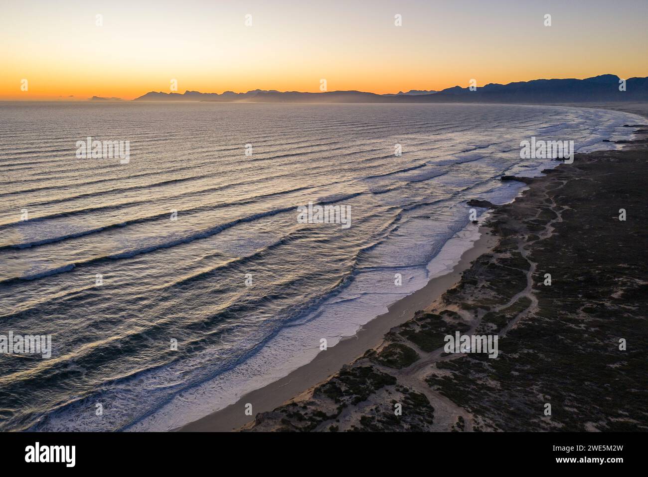 Vista aerea delle onde che si infrangono sulla costa e sulla spiaggia della riserva naturale di Walker Bay al tramonto, Gansbaai De Kelders, Western Cape, Sudafrica Foto Stock