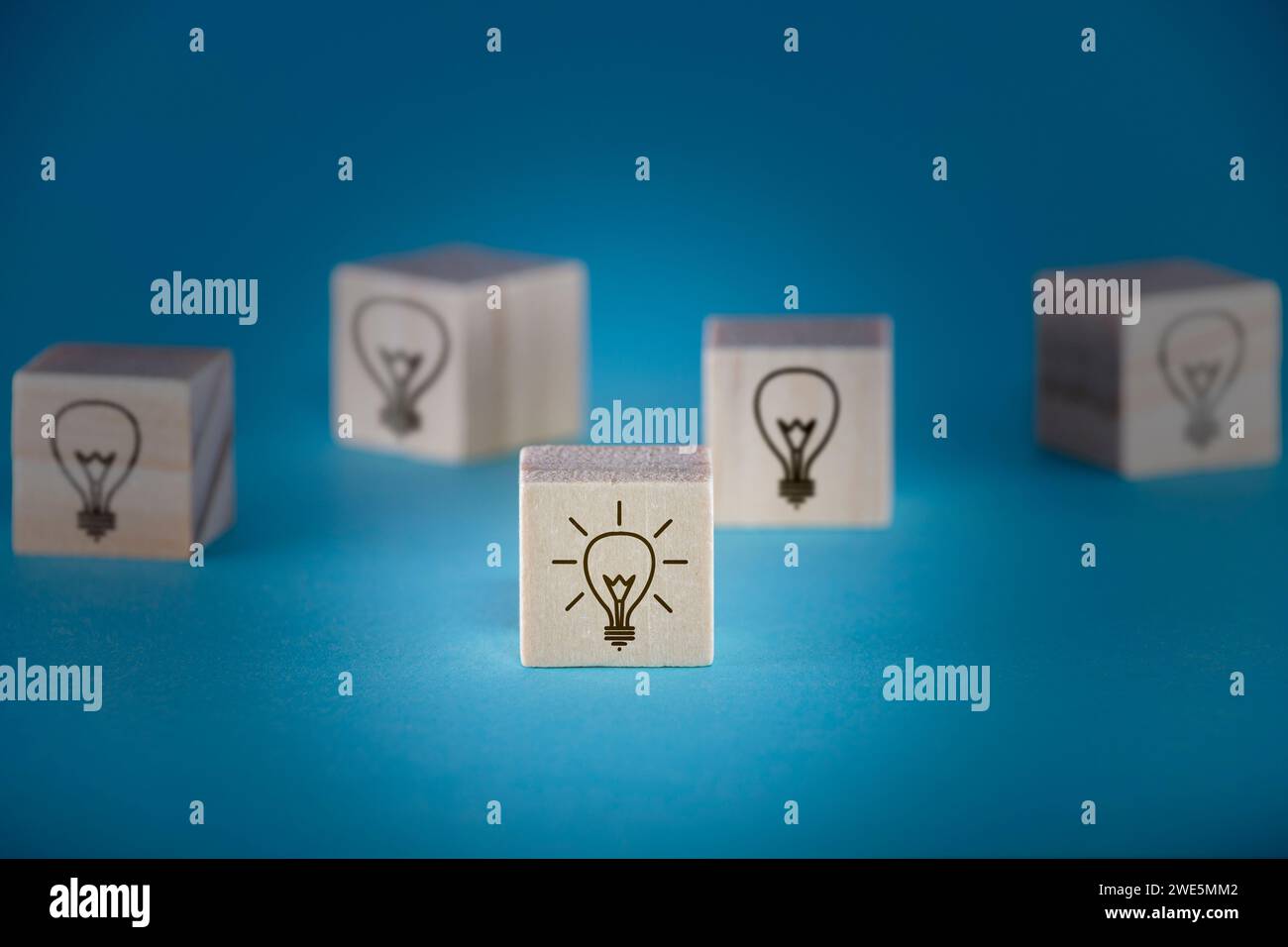 Più cubi di legno con icone di lampadine su sfondo blu profondo, uno dei quali è acceso, raffigurante brainstorming e sviluppo di concept. Foto Stock