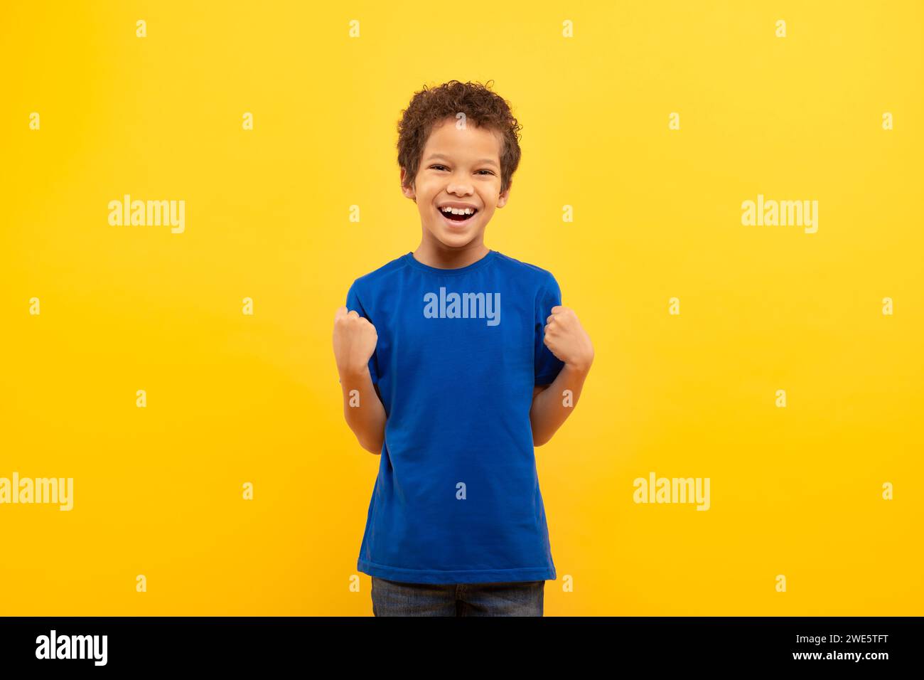 Ragazzo eccitato con pugni pompati in camicia blu su sfondo giallo Foto Stock