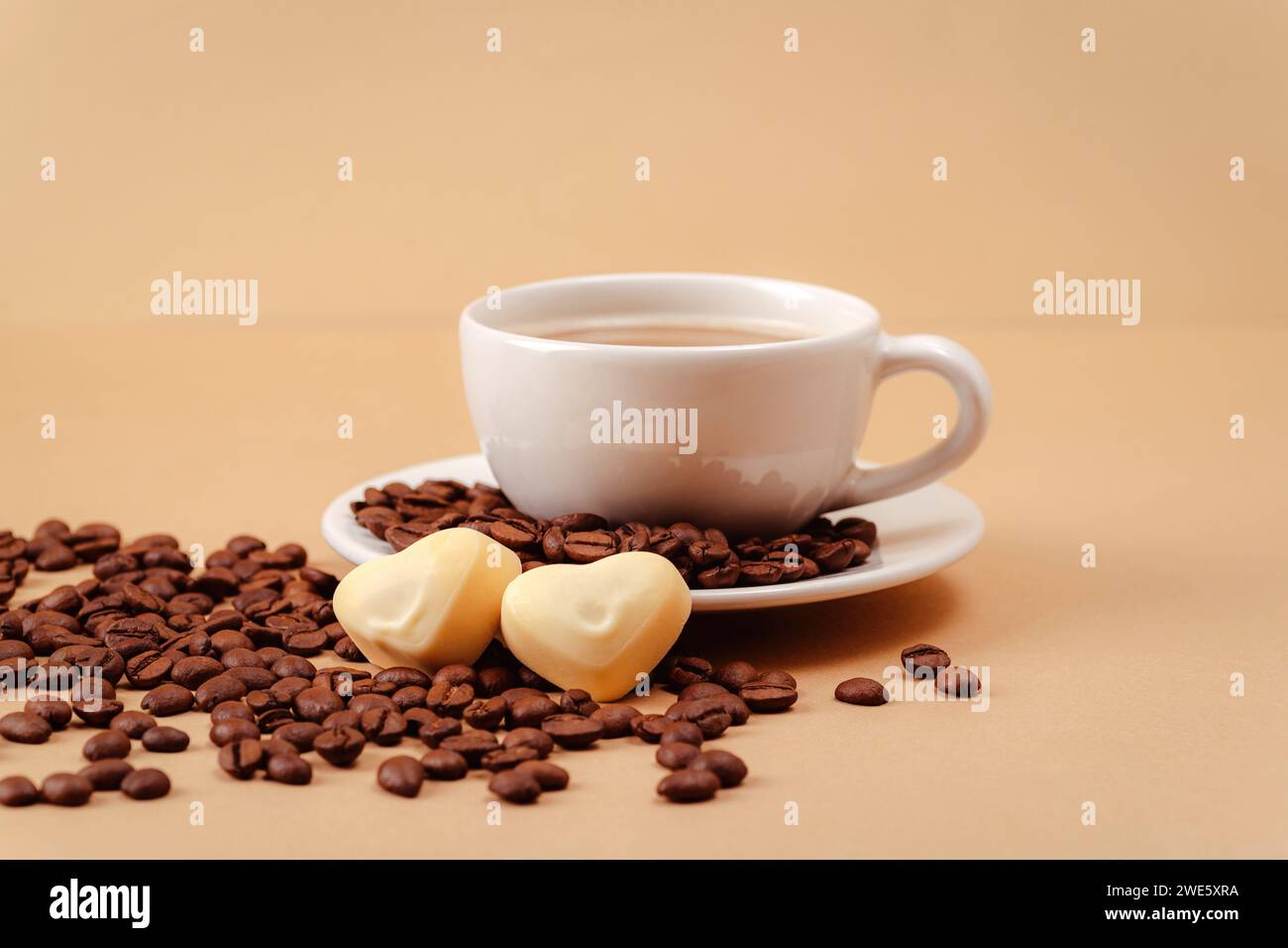 Tazza di caffè e chicchi di caffè, caramelle a forma di cuore e sfondo beige. Concetto di San Valentino. Primo piano. Foto Stock