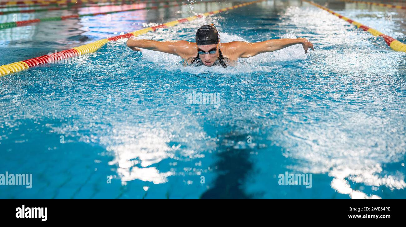 Vista frontale di una nuotatrice femminile che nuota in stile farfalla, un colpo che si esibisce in un nuoto competitivo. Concetto di successo, potenza e forza. Foto Stock