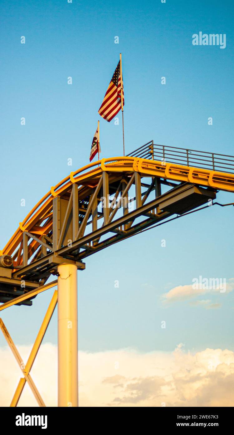 Pista delle montagne russe gialle con bandiera americana e bandiera californiana in cima Foto Stock