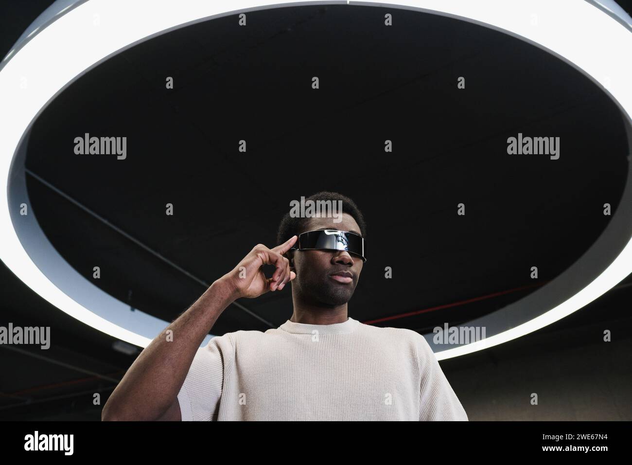 Giovane con futuristici bicchieri cyber sotto una moderna lampada ad anello con dito sulle stanghette Foto Stock