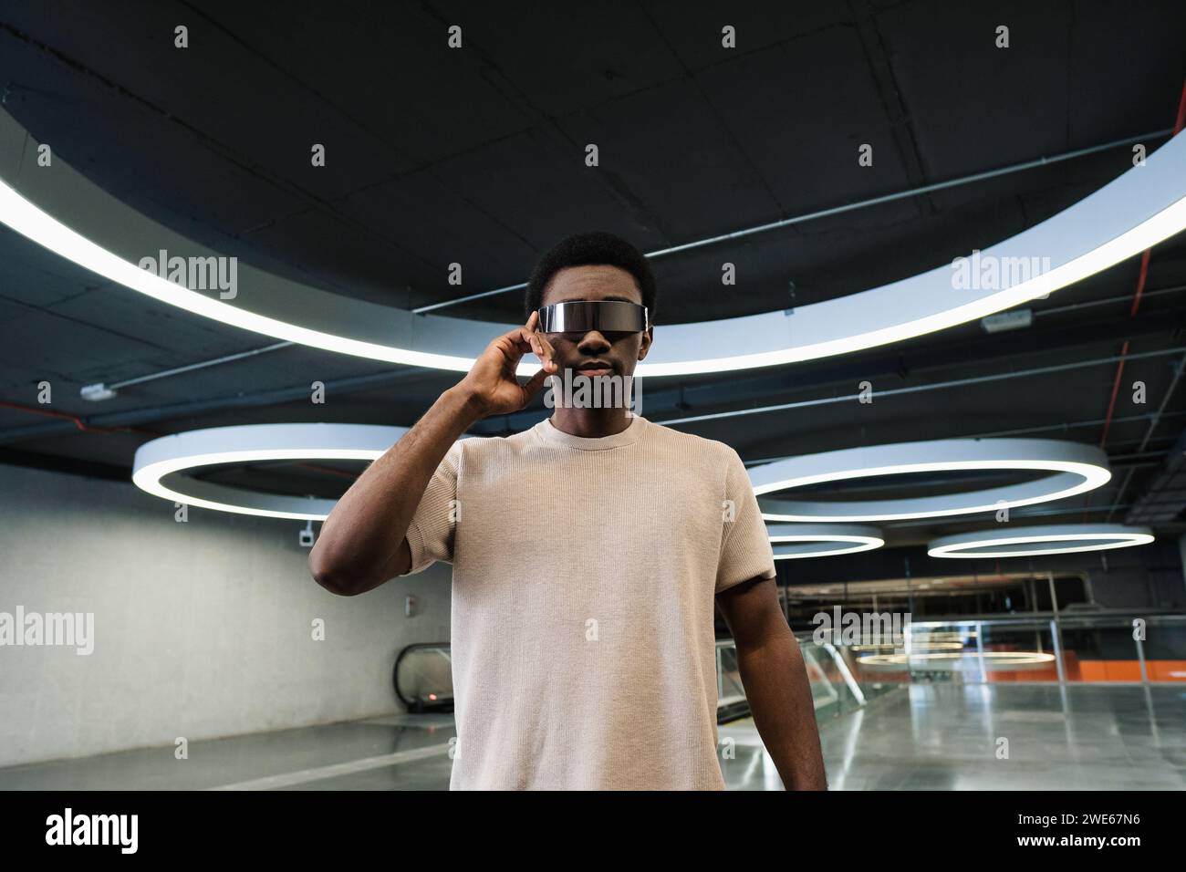 Giovane con futuristici bicchieri cyber sotto una moderna lampada ad anello con dito sulle stanghette Foto Stock