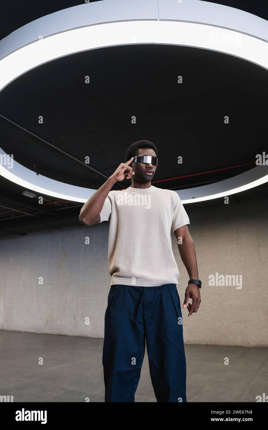 Giovane con futuristici bicchieri cyber sotto una moderna lampada ad anello con dito sulle stanghette Foto Stock