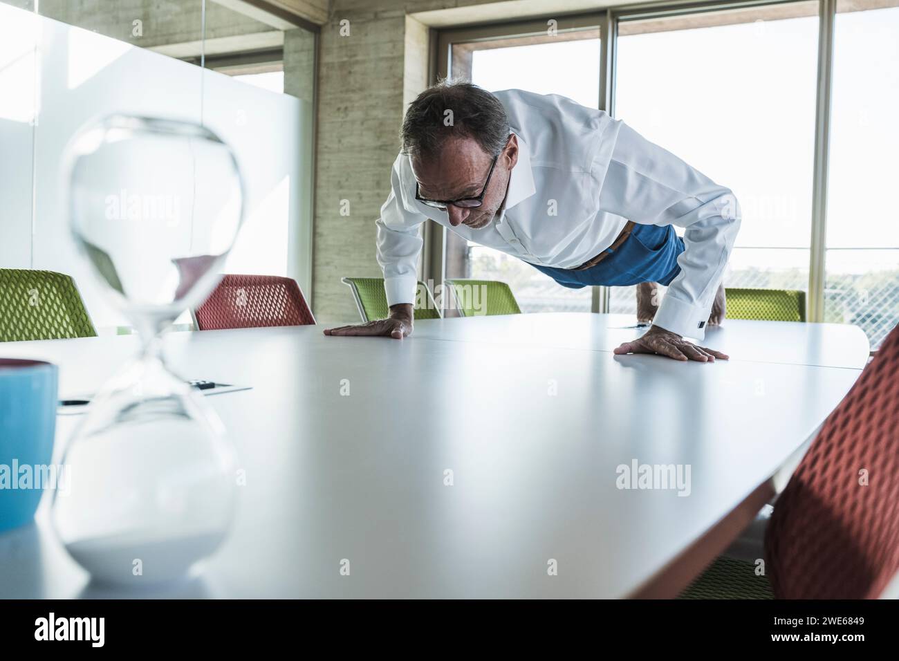 Uomo d'affari anziano che fa flessioni sulla scrivania in ufficio Foto Stock